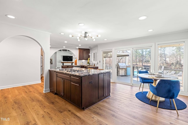 kitchen featuring crown molding, stainless steel gas cooktop, light wood-style flooring, dark brown cabinets, and dark stone counters