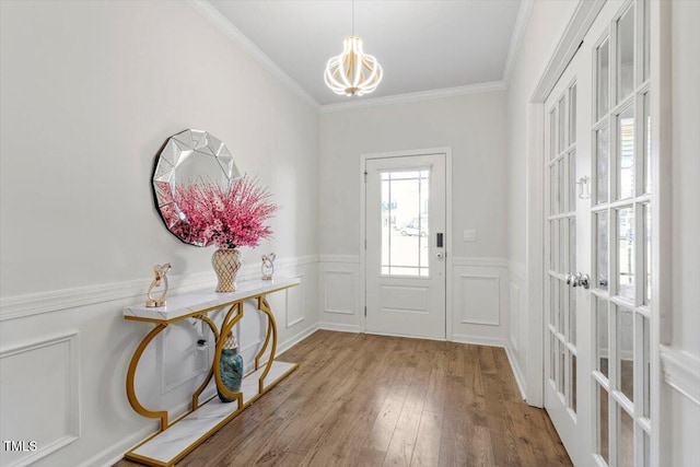 entryway featuring a decorative wall, crown molding, wood finished floors, wainscoting, and an inviting chandelier