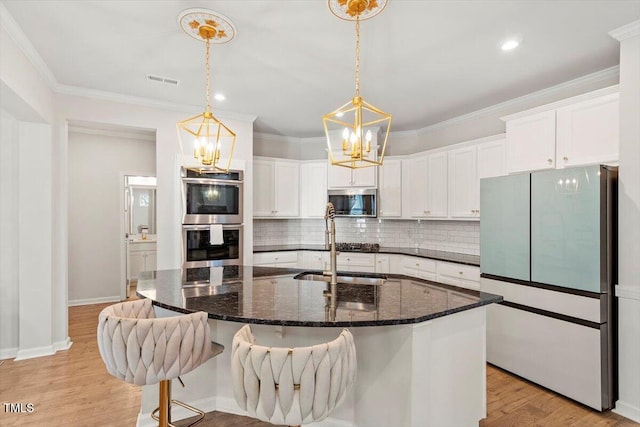 kitchen with stainless steel appliances, white cabinets, light wood-style floors, tasteful backsplash, and crown molding