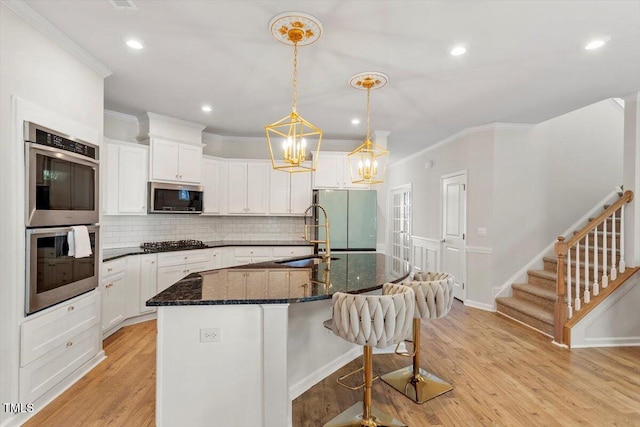 kitchen with a sink, appliances with stainless steel finishes, light wood-type flooring, decorative backsplash, and crown molding