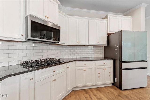 kitchen with ornamental molding, white cabinets, stainless steel microwave, and gas stovetop