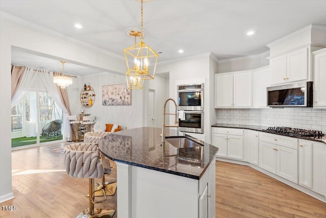 kitchen with appliances with stainless steel finishes, dark stone counters, light wood-type flooring, and a sink