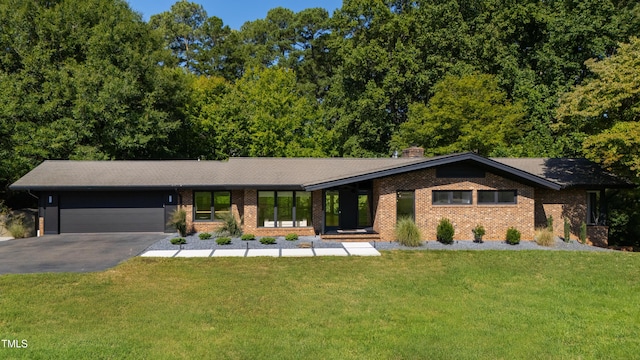 view of front of house with aphalt driveway, brick siding, a chimney, an attached garage, and a front yard