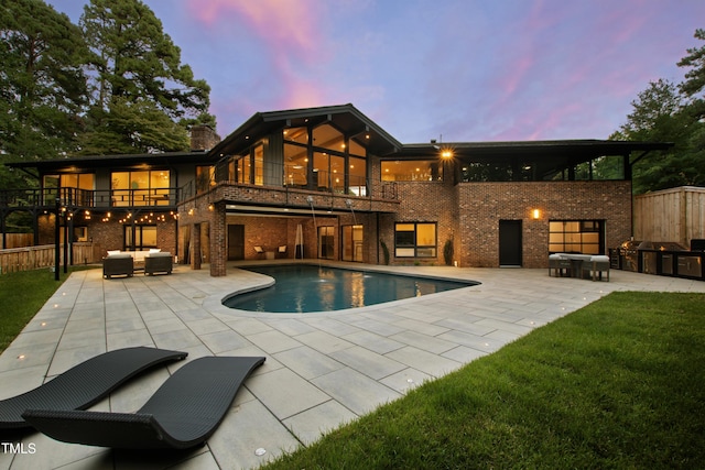 back of property at dusk featuring a patio, a balcony, area for grilling, and fence