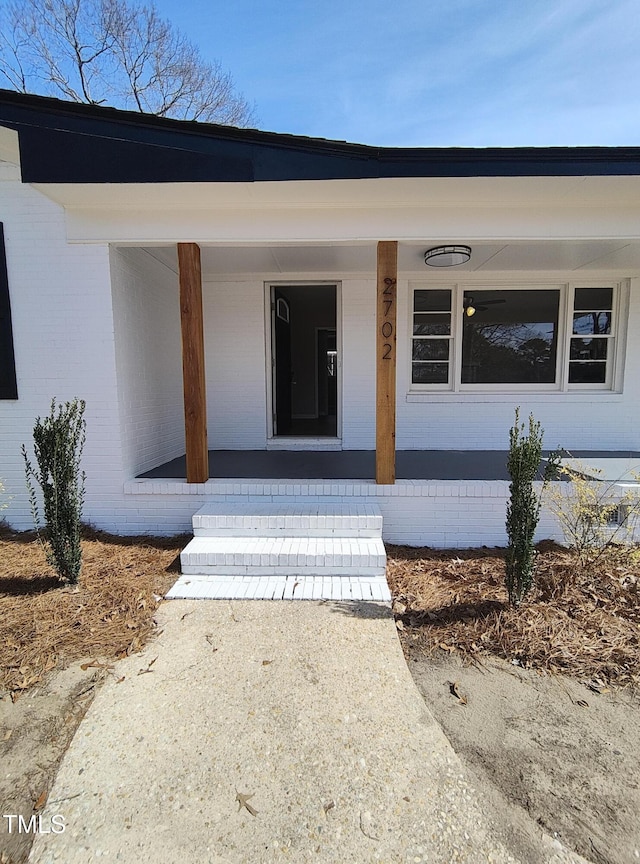 doorway to property featuring a porch and brick siding