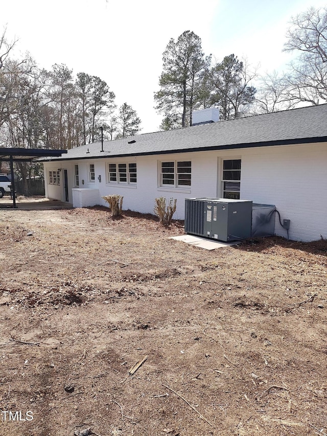 rear view of house with a shingled roof, an attached carport, brick siding, and central AC