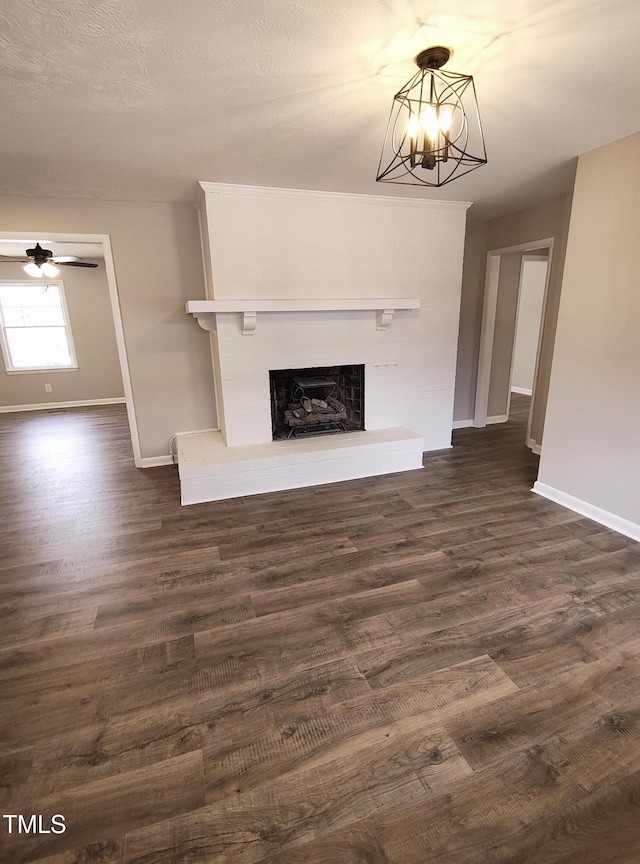 unfurnished living room with a fireplace with raised hearth, a textured ceiling, ceiling fan with notable chandelier, baseboards, and dark wood-style floors