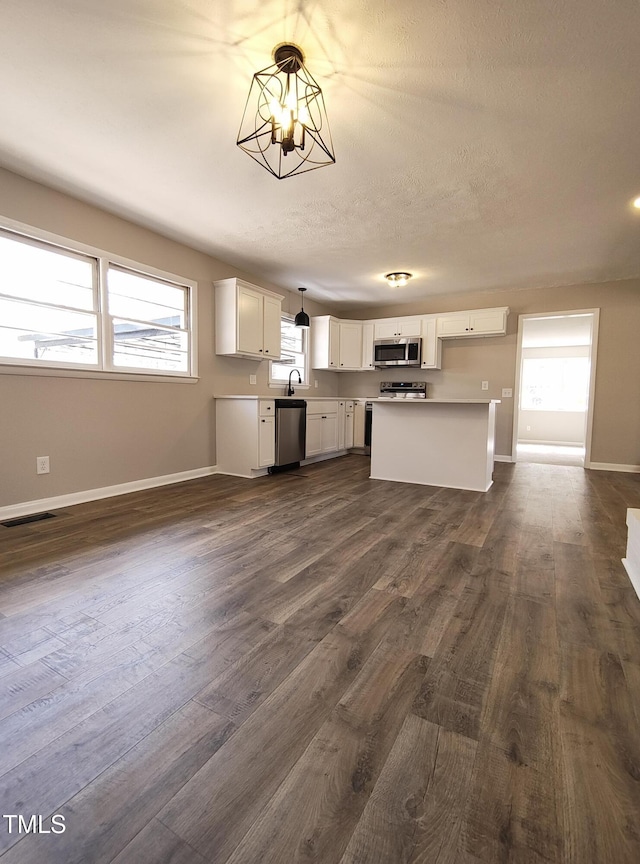 kitchen with a notable chandelier, appliances with stainless steel finishes, dark wood-type flooring, white cabinets, and baseboards