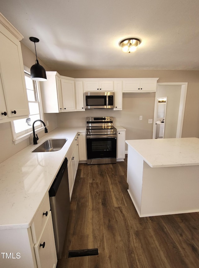 kitchen featuring dark wood-style flooring, hanging light fixtures, appliances with stainless steel finishes, a sink, and washer / dryer