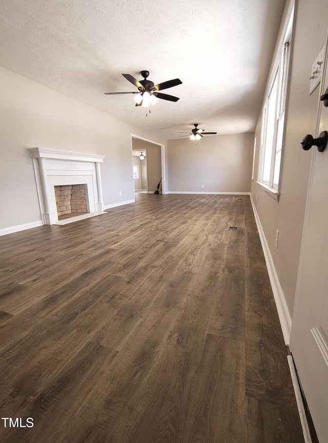 unfurnished living room featuring a textured ceiling, baseboards, a fireplace, and dark wood-style flooring