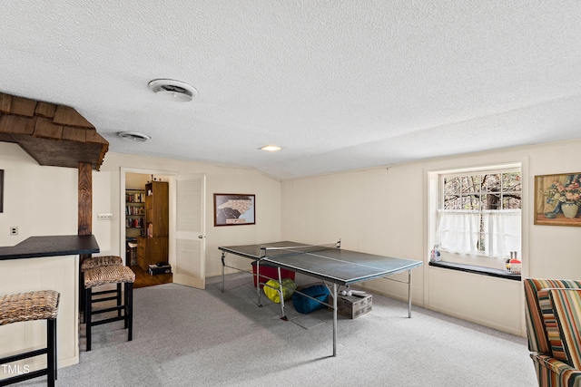 recreation room with carpet, visible vents, vaulted ceiling, and a textured ceiling