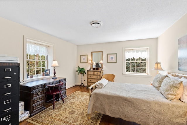 bedroom featuring a textured ceiling, multiple windows, a wall unit AC, and wood finished floors