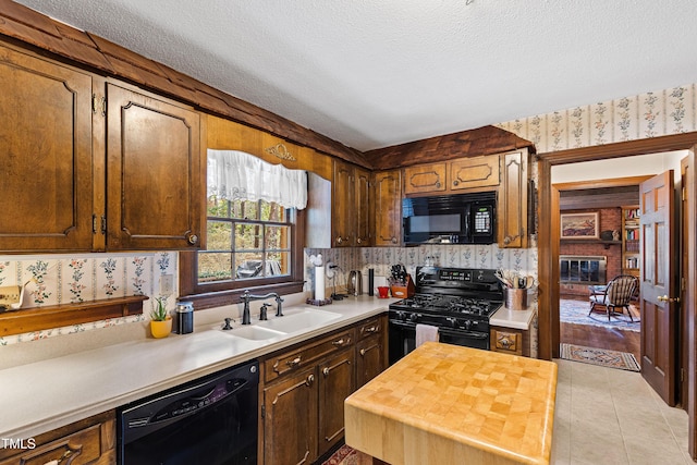 kitchen with a sink, a textured ceiling, black appliances, and wallpapered walls