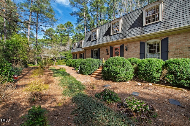 exterior space featuring brick siding and roof with shingles