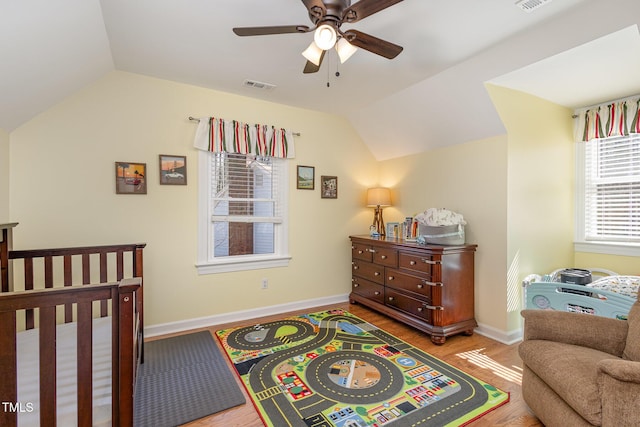 bedroom with baseboards, visible vents, lofted ceiling, wood finished floors, and a nursery area