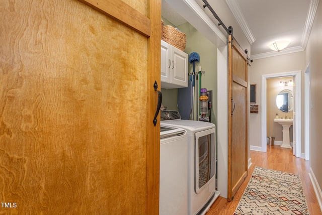 laundry area featuring crown molding, washer and clothes dryer, light wood finished floors, cabinet space, and a barn door