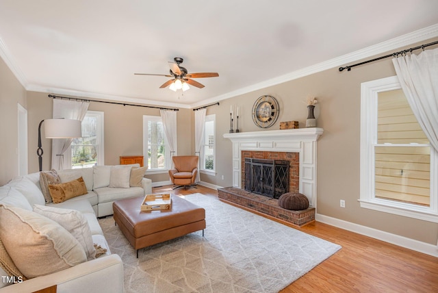 living room with baseboards, ceiling fan, wood finished floors, crown molding, and a brick fireplace