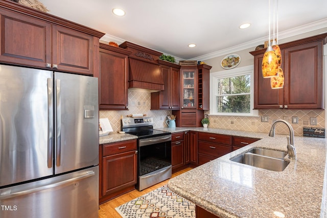 kitchen featuring stainless steel appliances, premium range hood, a sink, hanging light fixtures, and light wood-type flooring