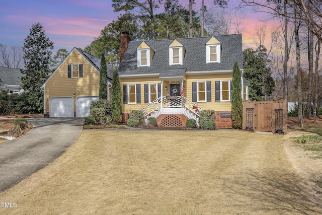 cape cod house featuring a yard, a chimney, a shingled roof, an attached garage, and driveway