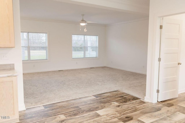 spare room with light wood finished floors, baseboards, a ceiling fan, light colored carpet, and crown molding