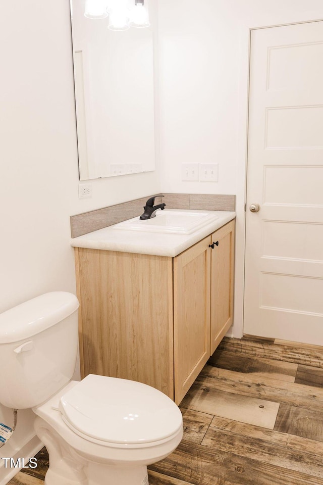 half bathroom with toilet, wood finished floors, and vanity