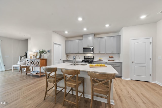 kitchen featuring decorative backsplash, gray cabinets, stainless steel appliances, light wood-type flooring, and a sink