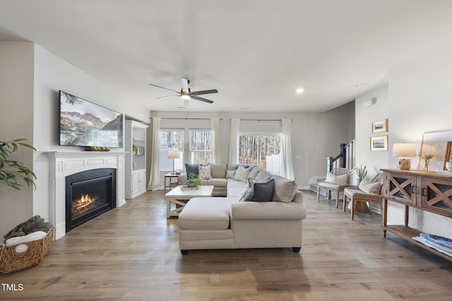 living room with light wood-style floors, stairs, a ceiling fan, and a glass covered fireplace