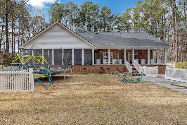 rear view of house featuring a lawn, a sunroom, crawl space, a trampoline, and fence