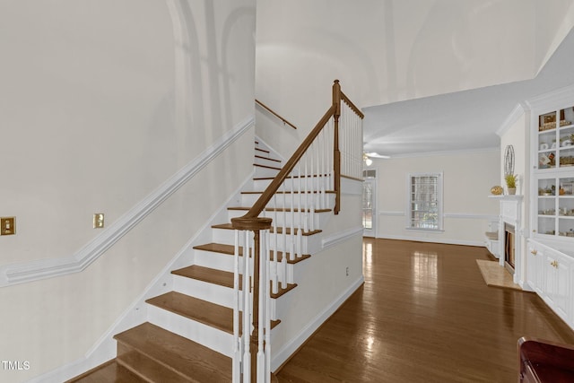 stairs featuring a fireplace with flush hearth, ornamental molding, and wood finished floors