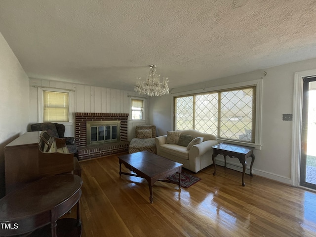 living room with a textured ceiling, a fireplace, wood finished floors, baseboards, and an inviting chandelier