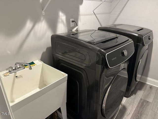 laundry area with laundry area, baseboards, wood finished floors, washer and dryer, and a sink