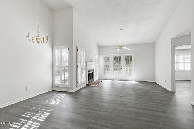 unfurnished living room with a fireplace with raised hearth, baseboards, dark wood finished floors, and ceiling fan with notable chandelier