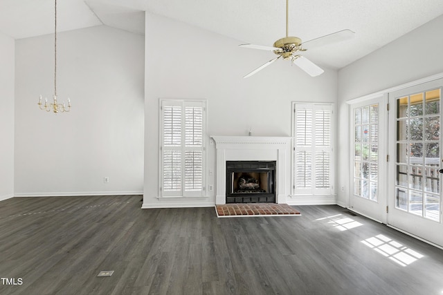 unfurnished living room featuring dark wood-style flooring, a fireplace with raised hearth, high vaulted ceiling, baseboards, and ceiling fan with notable chandelier