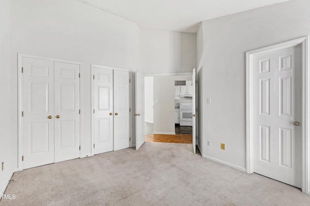 unfurnished bedroom with a towering ceiling, two closets, baseboards, and carpet flooring