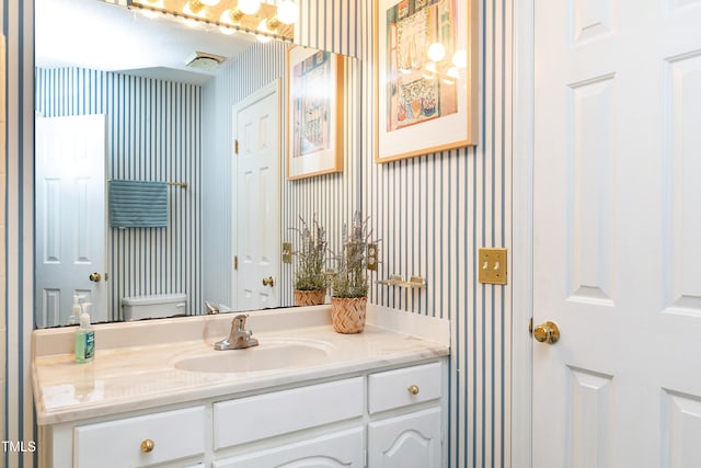 bathroom featuring toilet, wallpapered walls, and vanity