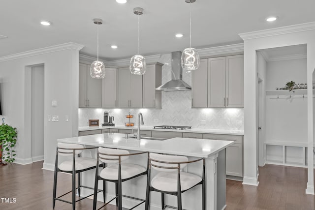 kitchen featuring gray cabinetry, a sink, light countertops, wall chimney exhaust hood, and a kitchen bar