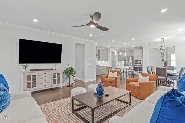 living room with recessed lighting, ceiling fan with notable chandelier, wood finished floors, baseboards, and ornamental molding