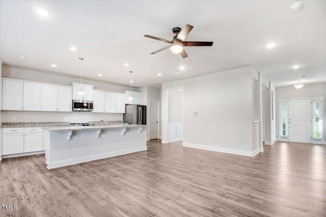 kitchen with appliances with stainless steel finishes, light wood-type flooring, open floor plan, and a kitchen island with sink