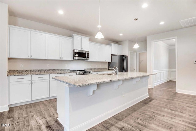 kitchen featuring a sink, visible vents, white cabinetry, appliances with stainless steel finishes, and an island with sink