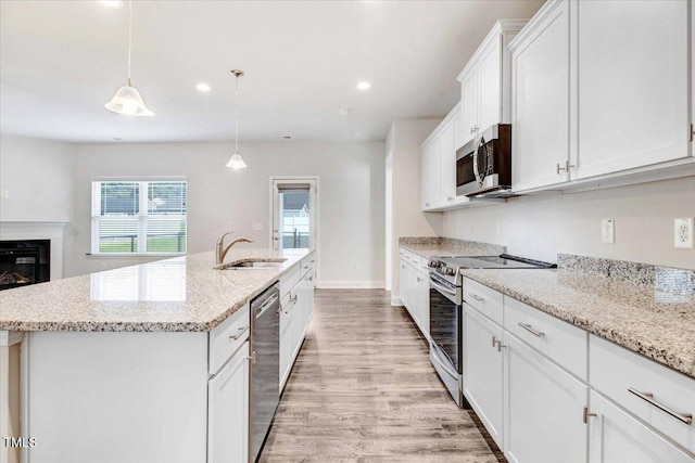 kitchen with light wood-style flooring, a kitchen island with sink, stainless steel appliances, white cabinetry, and a sink