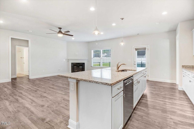 kitchen with light wood finished floors, dishwasher, a glass covered fireplace, a kitchen island with sink, and a sink