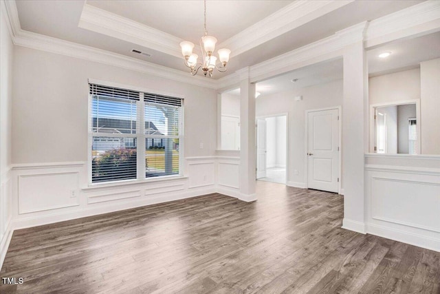 unfurnished dining area with a tray ceiling, crown molding, a notable chandelier, visible vents, and wood finished floors