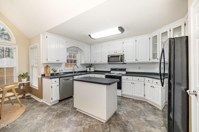 kitchen with appliances with stainless steel finishes, dark countertops, a sink, and white cabinetry