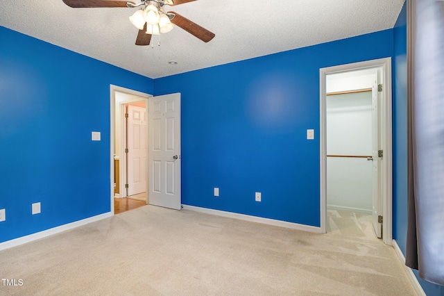 unfurnished bedroom featuring baseboards, a ceiling fan, carpet, a spacious closet, and a textured ceiling