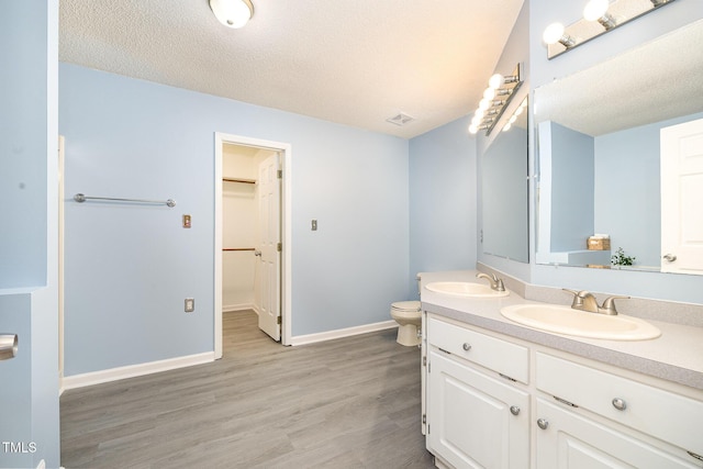 full bath featuring double vanity, a sink, toilet, and wood finished floors