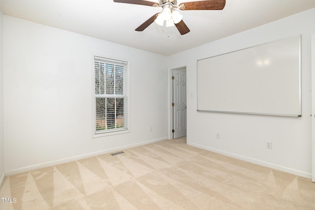 spare room featuring light colored carpet, ceiling fan, visible vents, and baseboards