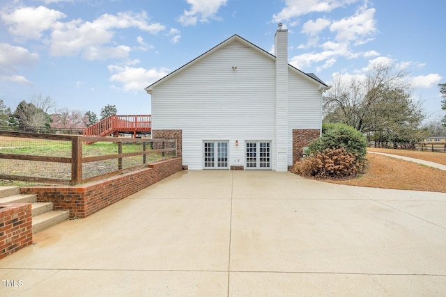 view of side of home featuring french doors, a chimney, and fence