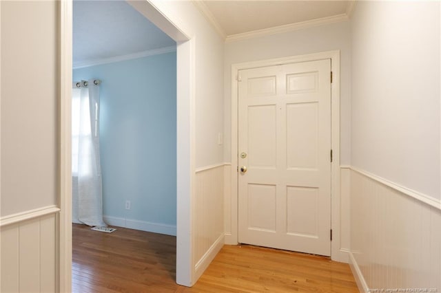 hallway with a wainscoted wall, crown molding, visible vents, and light wood finished floors