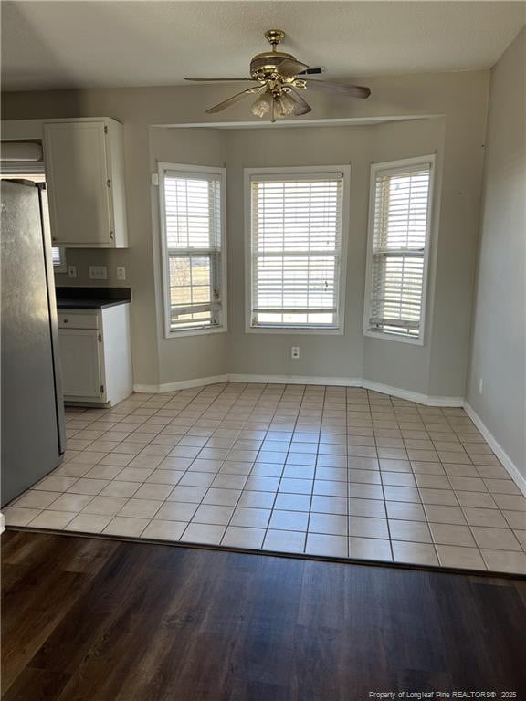 unfurnished dining area featuring baseboards, a ceiling fan, and light tile patterned flooring