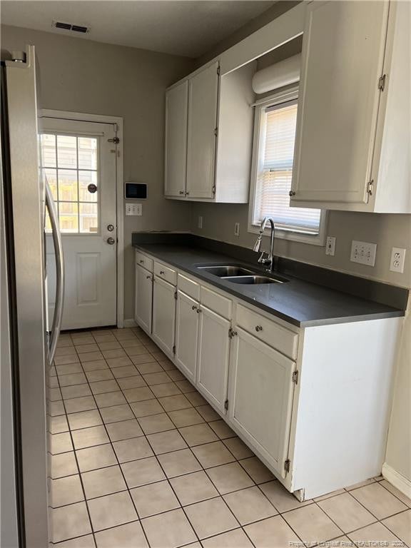 kitchen with a sink, visible vents, white cabinetry, freestanding refrigerator, and dark countertops